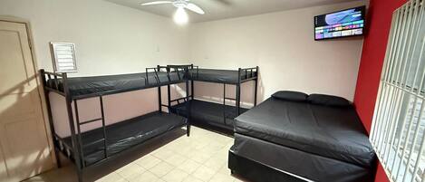 A dormitory room with bunk beds, a ceiling fan, a television, and a window with bars.