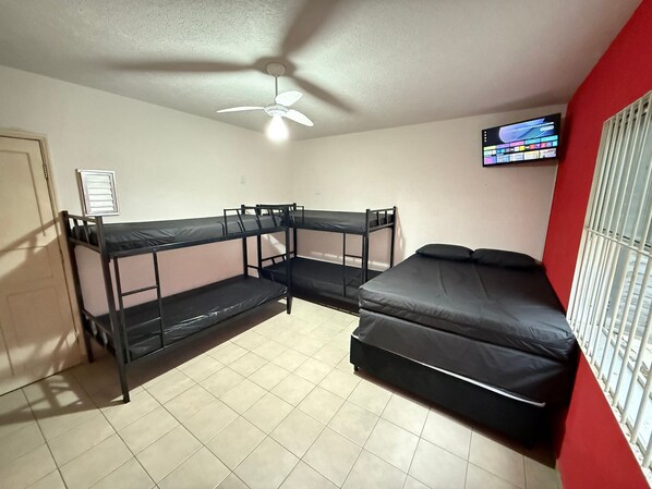 A dormitory room with bunk beds, a ceiling fan, a television, and a window with bars.