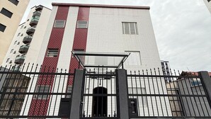Un edificio de varios pisos con fachada roja y blanca, una entrada protegida por una reja y vistas de otros edificios al fondo.
