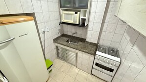 Una kitchenette compacta con un refrigerador blanco, un microondas, un fregadero y una estufa.