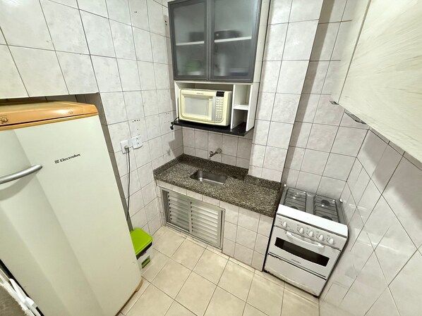 A compact kitchenette with a white refrigerator, a microwave, a sink, and a stove.