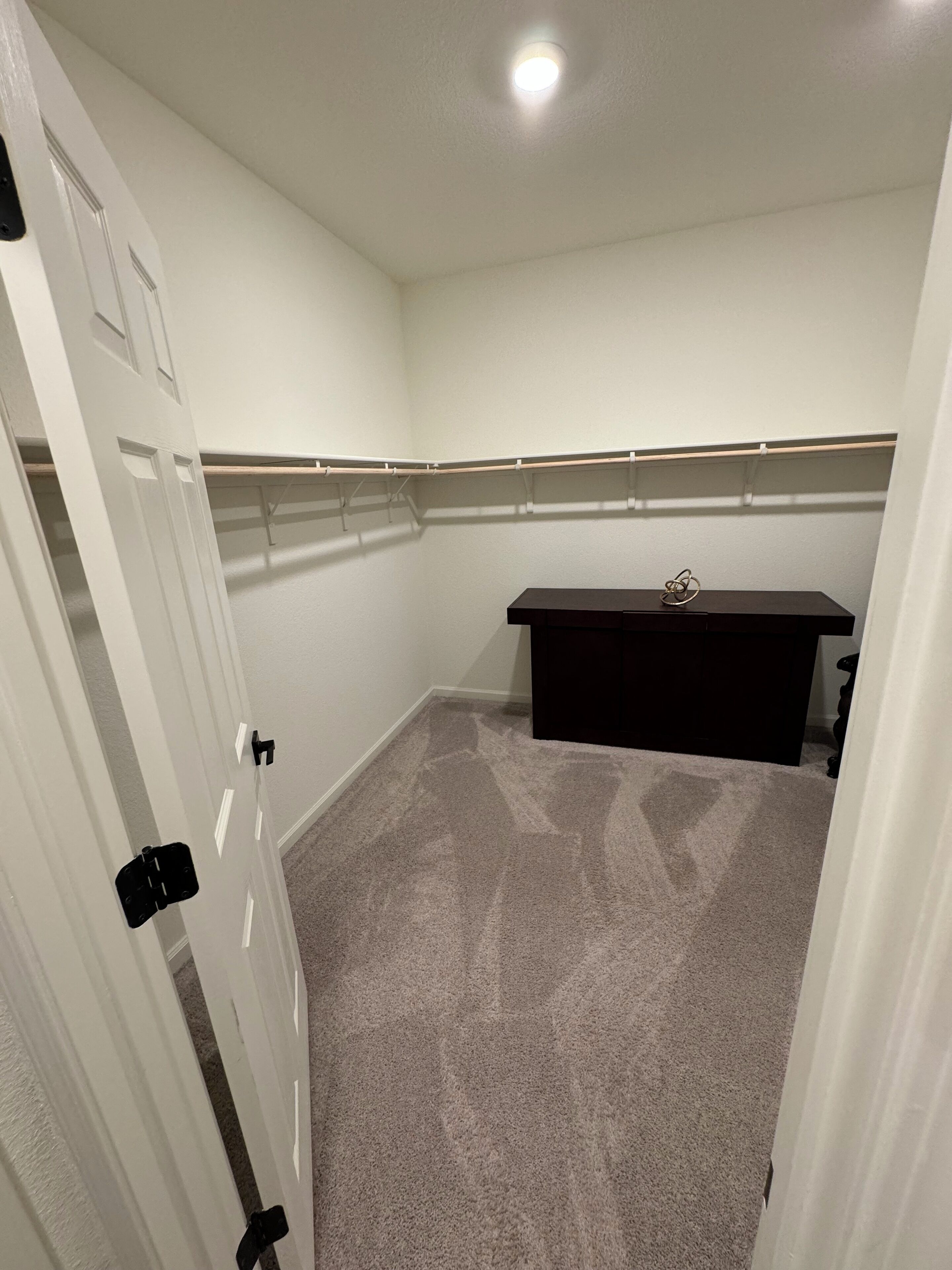 Una habitación con piso alfombrado, un escritorio de color oscuro y una puerta blanca.