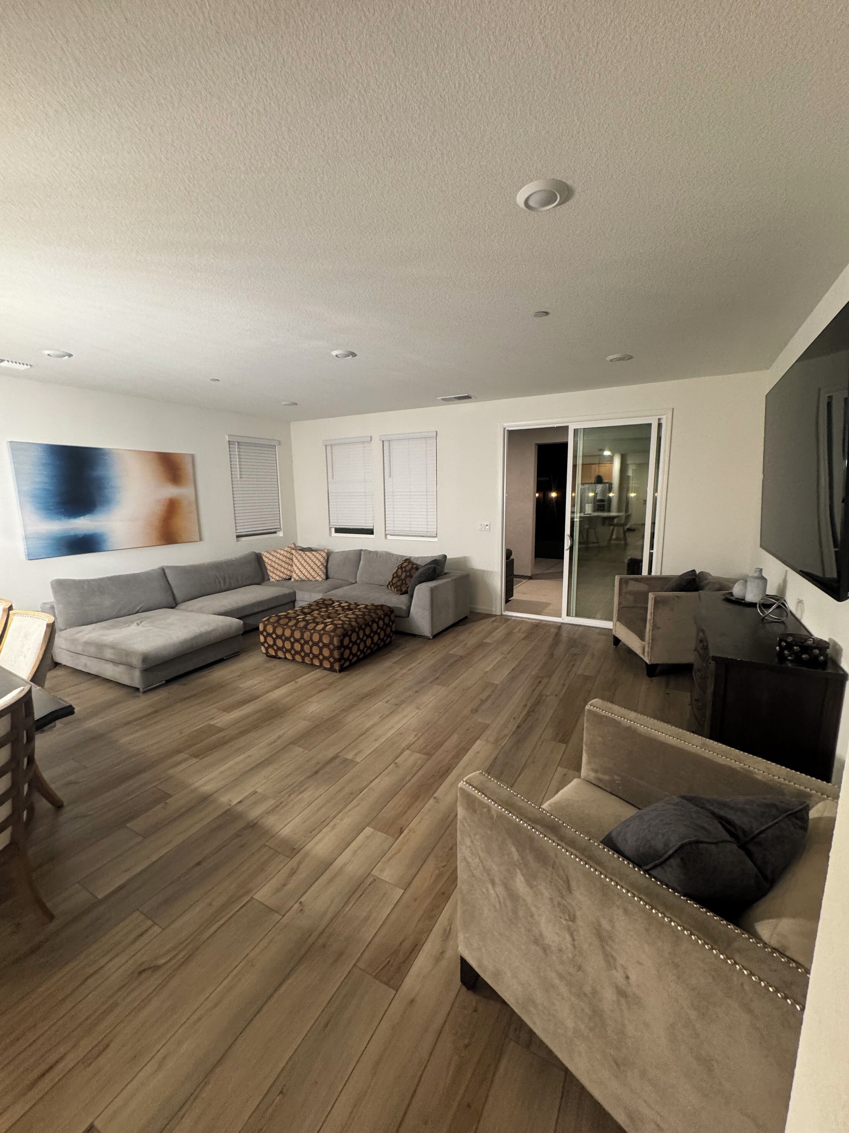 A modern living room with a grey sectional sofa, a patterned ottoman, and a beige armchair.
