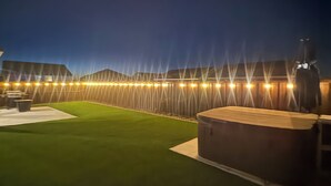 Une terrasse sur le toit, dotée d’un revêtement d’herbe artificielle, d’un espace salon et d’une rangée de lumières disposées à intervalles réguliers.