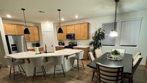 Une cuisine moderne avec des meubles en bois, un réfrigérateur en acier inoxydable, un four à micro-ondes et un îlot central doté de tabourets de bar.