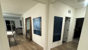 Un vaste couloir doté d’un plancher en bois, de murs blancs et d’un grand miroir. Deux œuvres d’art encadrées ornent les murs, et une porte donne accès à une autre pièce.