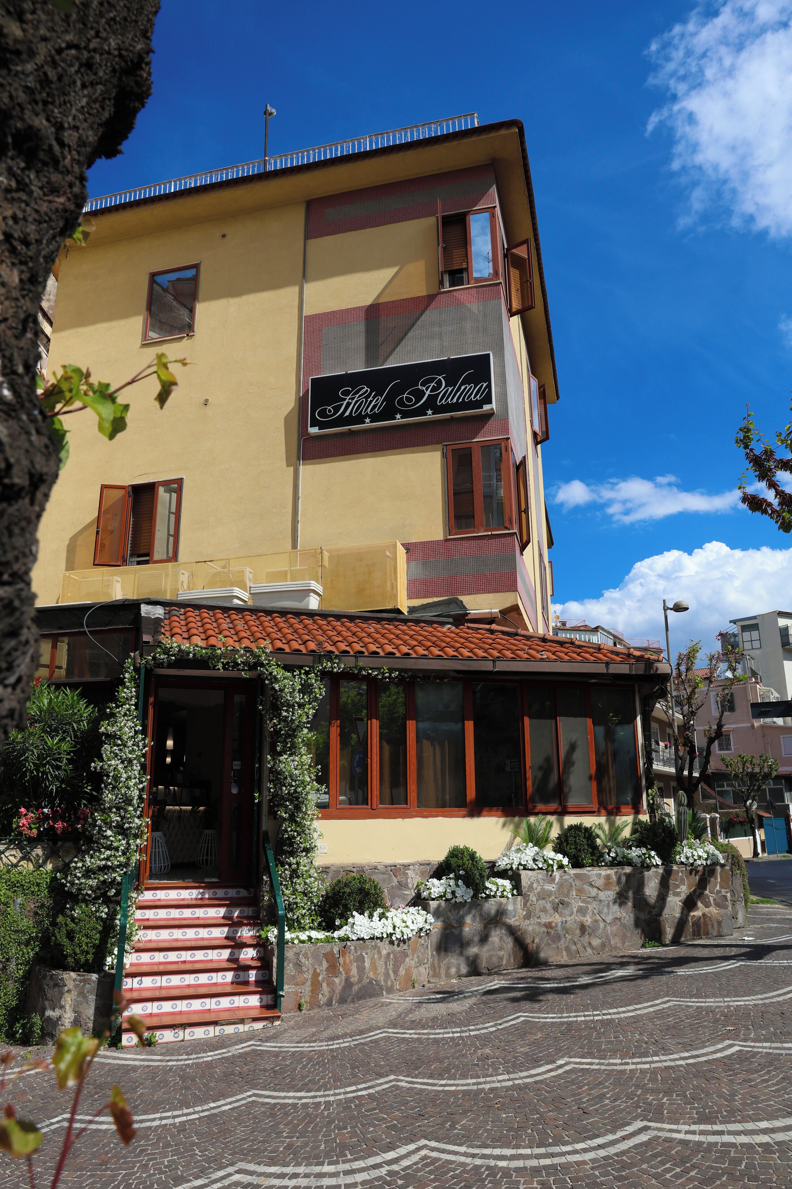 Ein zweistöckiges Gebäude mit der Aufschrift "Hotel Punta". Es hat ein Ziegeldach, eine Treppe mit roten und weißen Fliesen sowie eine Steinwand mit Pflanzen.