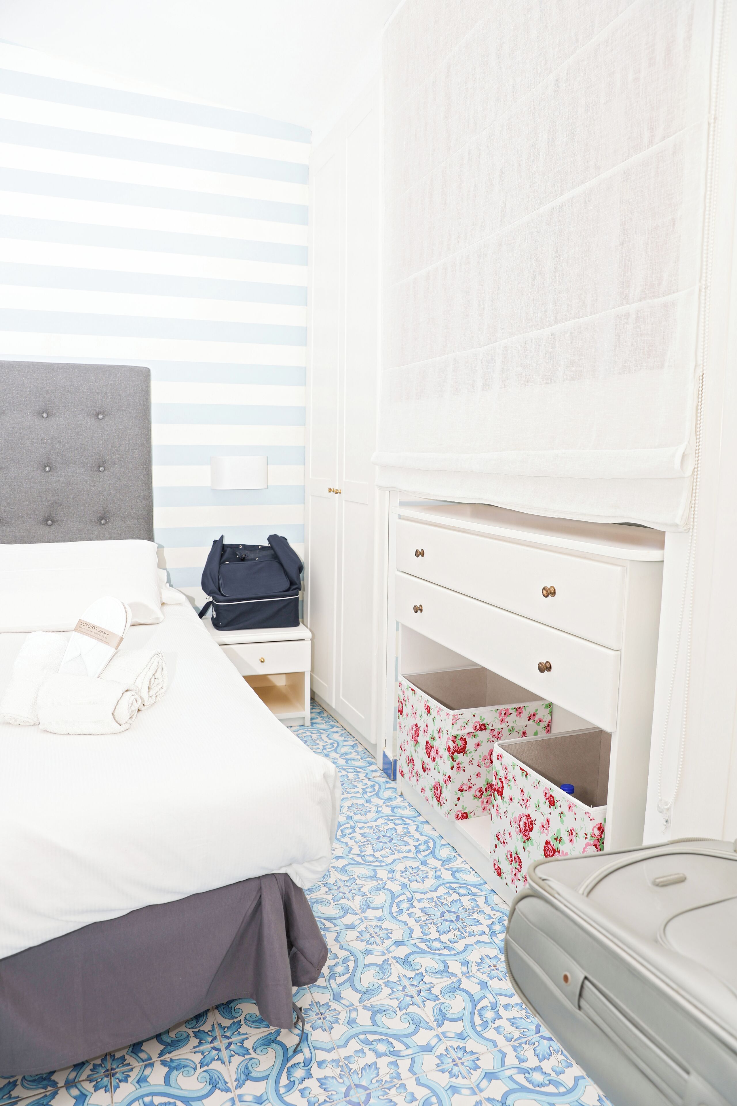 A hotel room with a bed, a nightstand, a dresser, and a suitcase.