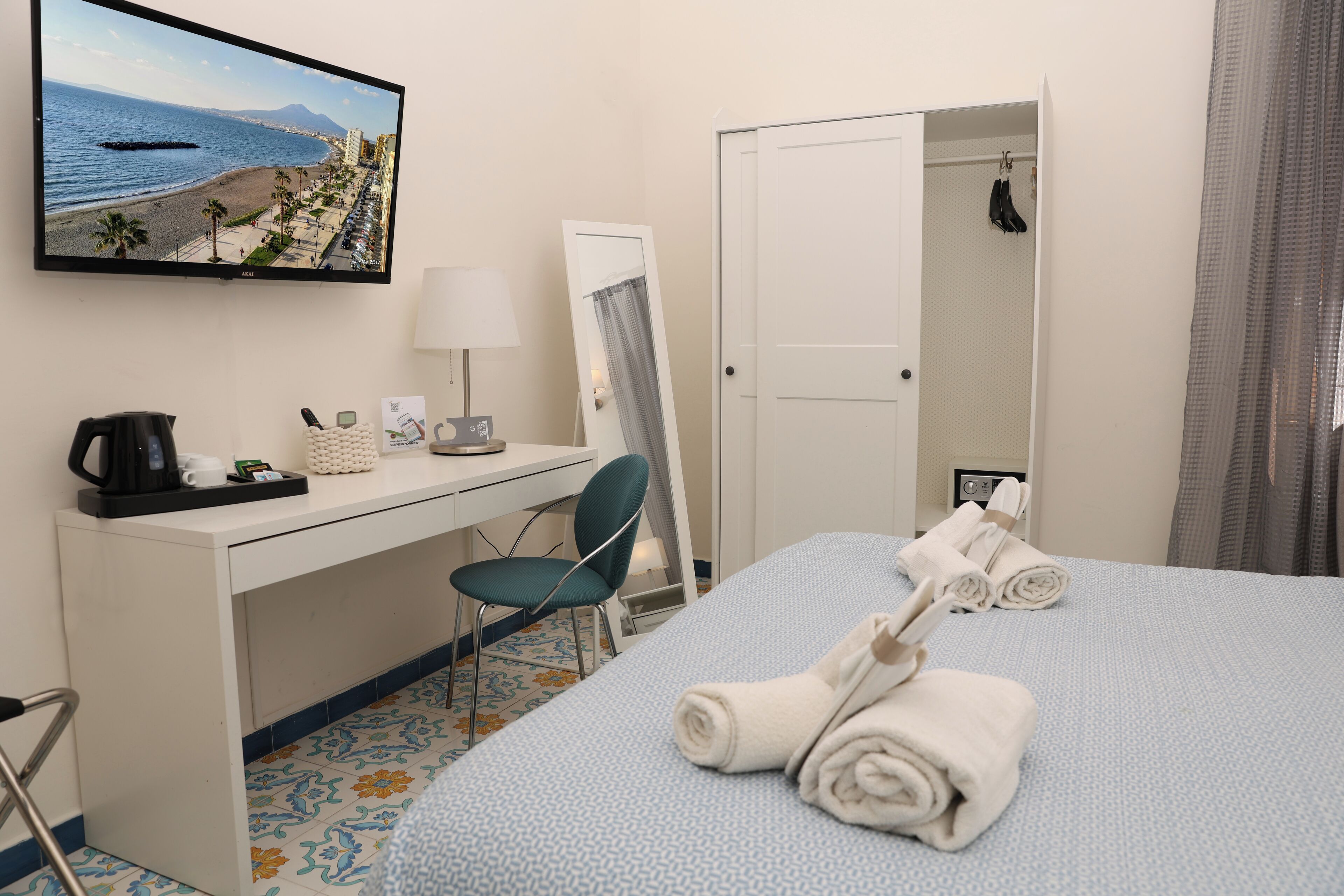 A hotel room with a bed, a desk, a chair, a TV, and a bathroom visible through an open door.