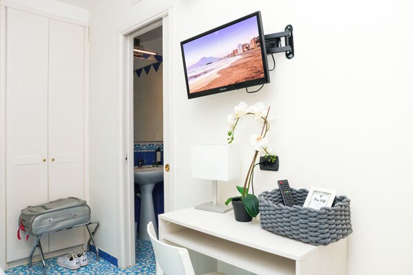 A hotel room with a mounted TV displaying a beach scene, a white desk with a potted plant, a remote control, and a 'Free Wifi' sign. - Hotel Palma Central (Castellammare di Stabia)
