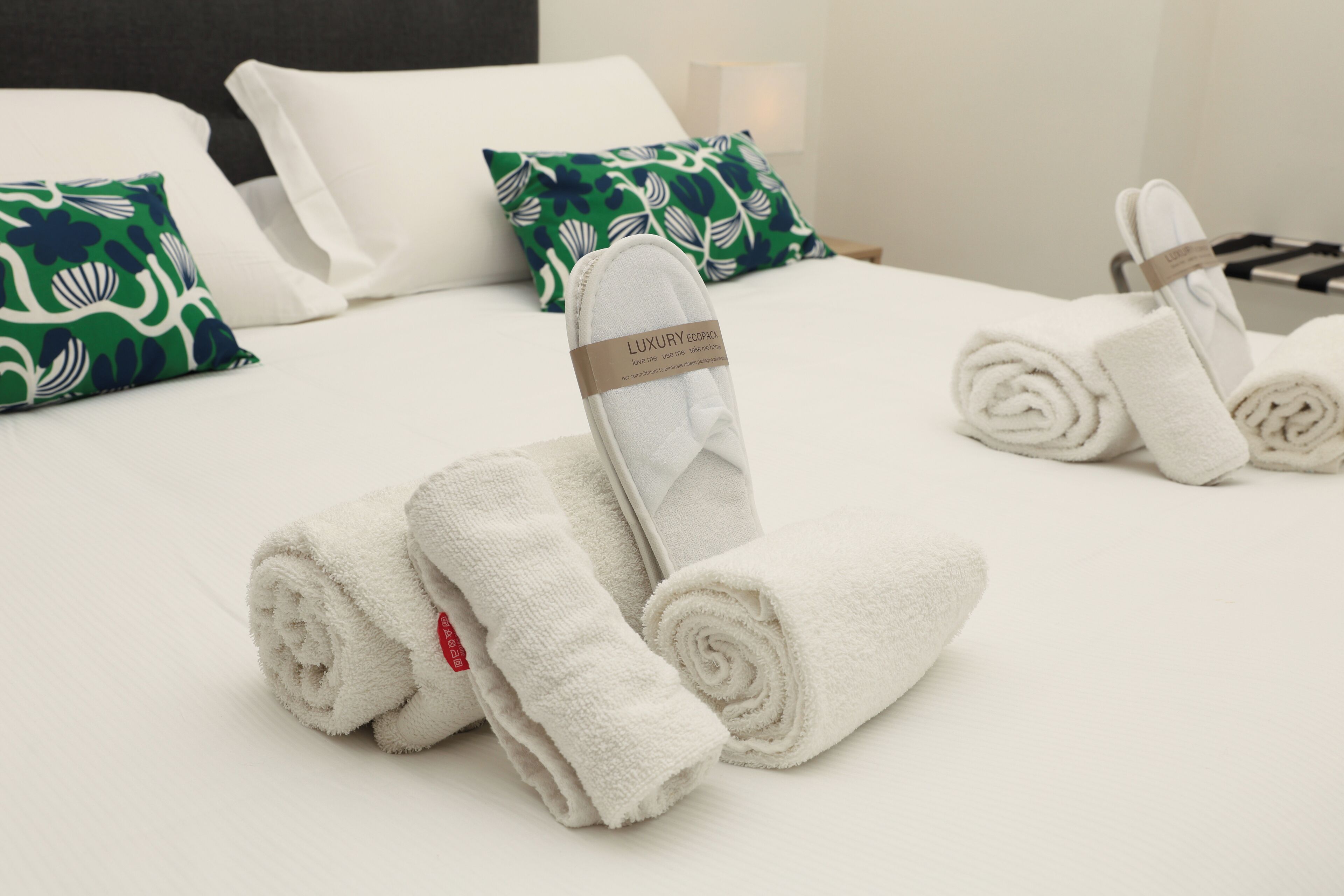 A neatly made bed with white linens, including rolled towels and a pillow with a green leaf pattern.