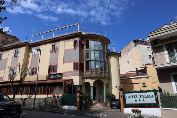 A hotel with a sign reading 'HOTEL PALMA,' a stone wall, a vehicle, and a clear sky.