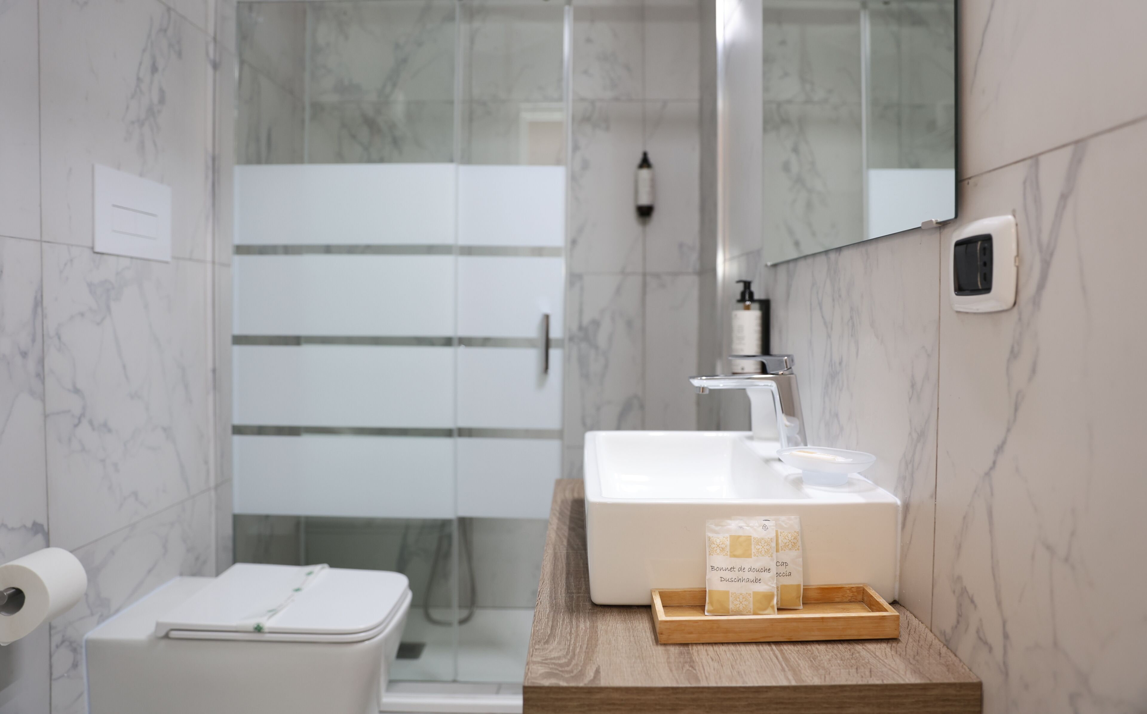 A modern bathroom with a glass shower enclosure, a white sink with a wooden tray, and a toilet with a lid.
