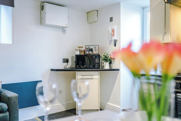 A compact kitchen with a microwave, a small refrigerator, and a white cabinet.