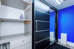 A room with a wardrobe, a radiator, and a shelf with an iron.
