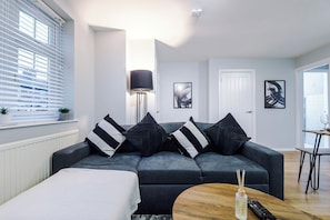 A modern living room with a grey sofa, black and white striped pillows, a standing floor lamp, and a wooden coffee table.
