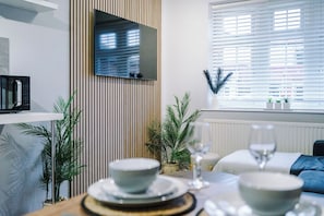 A modern dining area with a table set for two, a microwave on a shelf, and a window with blinds.