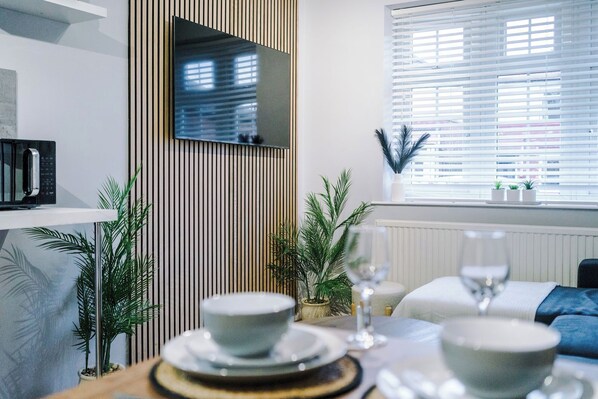 A modern dining area with a table set for two, a microwave on a shelf, and a window with blinds.