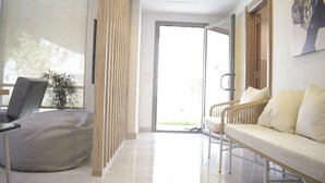Een moderne woonkamer met een bank, een fauteuil, een plant en een schuifpui die leidt naar een buitengebied.