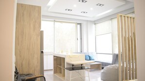 Een moderne, goed verlichte kamer met een groot raam, een bureau met stoel, een bank en een babyschommel.