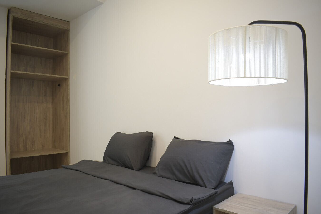 Un dormitorio con cama, dos almohadas, una mesita de noche, una lámpara y un armario de madera.