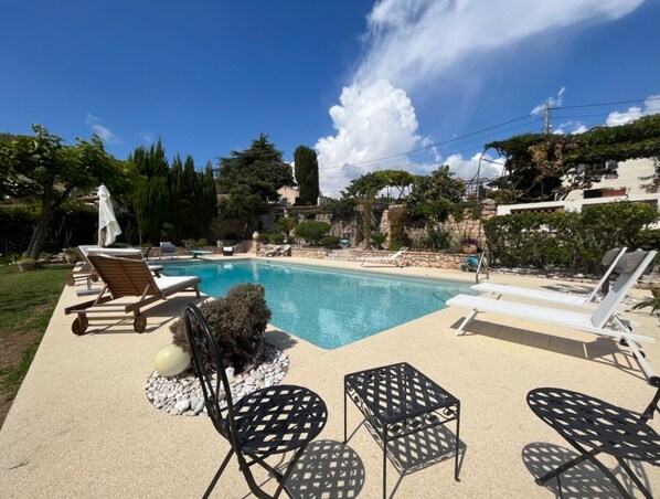 A swimming pool with lounge chairs and a small table, surrounded by greenery and a stone wall. - Le Mas des iris, large swimming pool, panoramic sea view, Cap d'Antibes beaches 5 minutes away (Antibes)