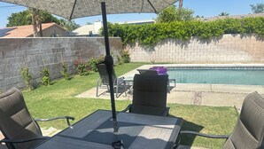 An outdoor patio with a table and chairs, a pool, and a covered area.