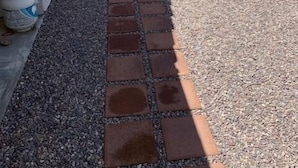 A narrow outdoor pathway with a brick and gravel surface, bordered by a wall on one side and a building on the other.