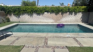 A rectangular swimming pool with clear blue water, surrounded by a stone border and a hedge.