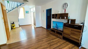 Un salon avec un plancher en bois, un téléviseur, une horloge et un escalier.
