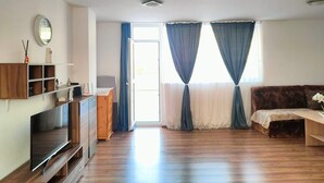 Un salon spacieux doté d’un plancher en bois, d’un téléviseur à écran plat posé sur un meuble en bois, d’un canapé, d’une table basse et d’une grande fenêtre agrémentée de rideaux.