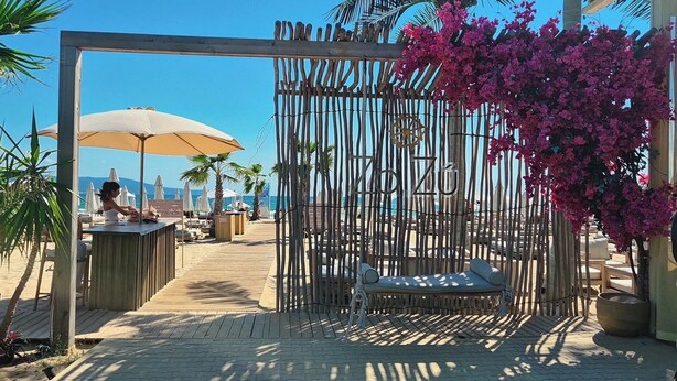 Une pergola en bois ornée de fleurs roses, une terrasse en bois et des parasols de plage.