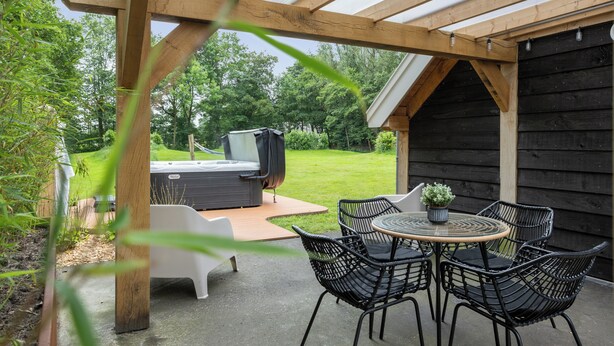 Een overdekt terras met een jacuzzi, buitenmeubels en uitzicht op een gazon.