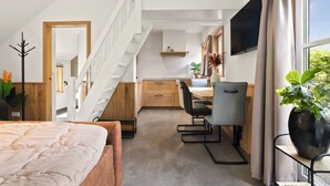 Een modern interieur met een trap naar een hoger niveau, een eetgedeelte met een tafel en stoelen, en een bed met hoofdeinde.