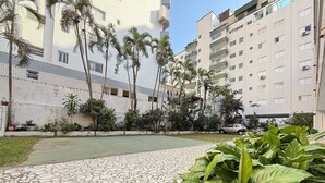 Un patio con suelo de baldosas, palmeras y un coche estacionado al fondo.
