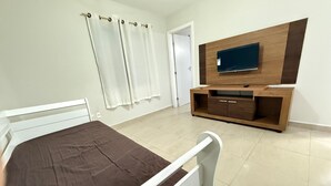 Un dormitorio con una cama, un televisor instalado en un mueble de madera y una puerta que da a otra habitación.
