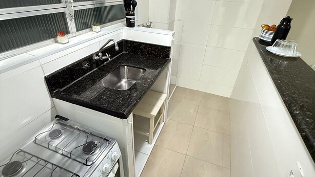 Cocina pequeña con estufa a gas, un lavamanos y una ventana con persianas.