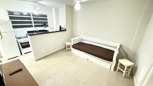Un espacio habitable compacto con kitchenette, cama y una mesita.