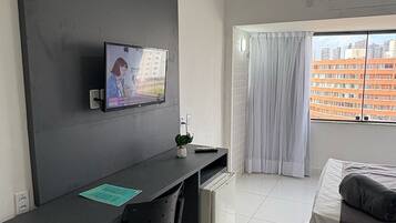 Un dormitorio moderno con cama, escritorio con silla, televisor montado en la pared y ventana con cortinas.