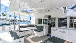 A yacht's deck with a seating area, a small table, and a galley with a sink and stove. - Stay Together, "Somewhere" - 4 Bed & 4 Bath - Catamaran in Key West (Key West)