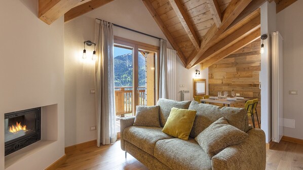A cozy living room with a fireplace, wooden beams, a sofa with cushions, and a dining area with a table and chairs. - Zarabella Delle Alpi (Temù)