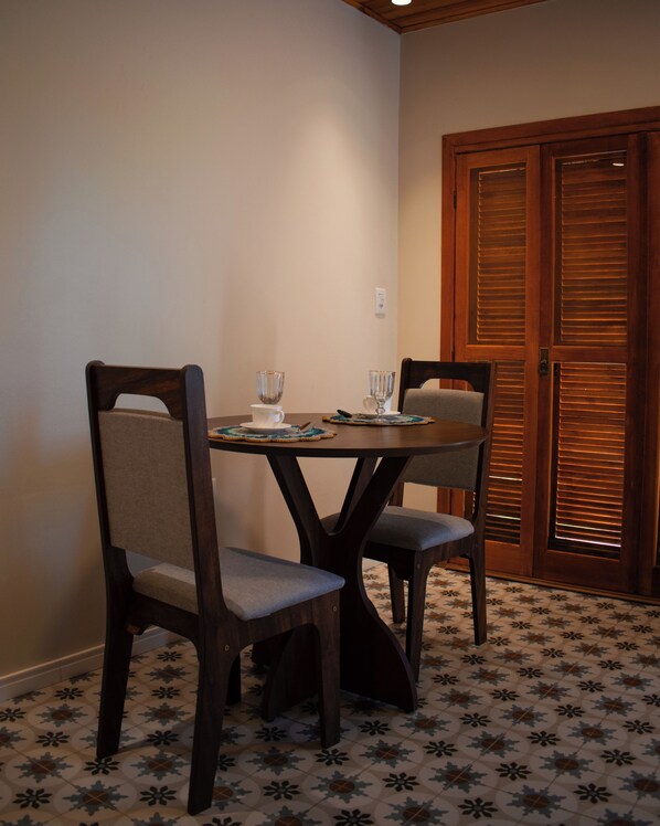 A dining area with a wooden table and chairs, a tiled floor, and a wooden door with shutters. - Celeste Suites, in Vale dos Vinhedos with Bathtub and Colonial Breakfast (Vale dos Vinhedos)