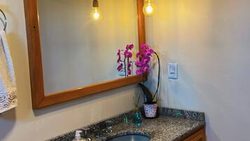 A bathroom with a granite countertop sink, wooden cabinetry, a mirror with a wooden frame, and two exposed light bulbs.