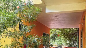 A covered outdoor area with yellow walls, potted plants, and a red chair.