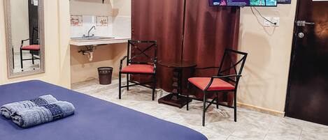 A hotel room with a bed, two chairs, a small table, a sink, and a TV mounted on the wall.