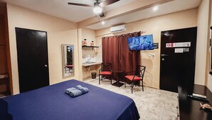 A hotel room with a bed, a desk, a chair, a television, and an air conditioning unit.