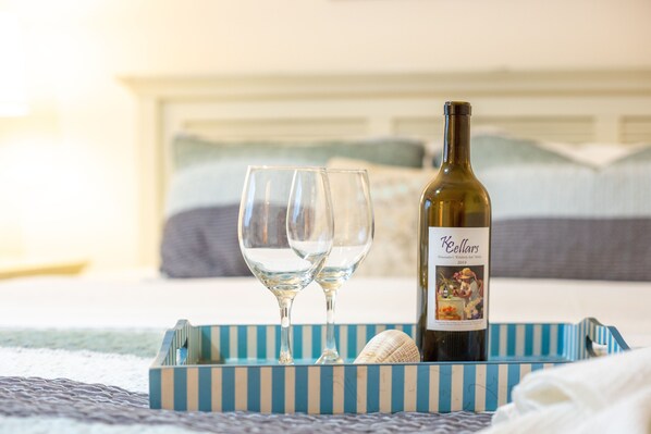 Un lit avec une tête de lit bleue et blanche à rayures, deux verres à vin vides et une bouteille de vin Keellars sur un plateau assorti.