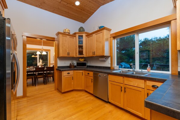 A modern kitchen with wooden cabinets, a dishwasher, and a large window. - Upscale Beach Retreat * KC's Serenity By The Sea (Warrenton)