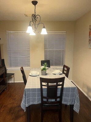 A dining area with a table set for four, two chairs on each side, a chandelier, and a window with blinds. - Spacious 3 Bed/2Bath House in Conroe (Conroe)