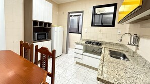 A compact kitchen with white cabinets, a microwave, a refrigerator, a gas stove, and a sink. - Pé na Areia Canto do Forte VI (Praia Grande)